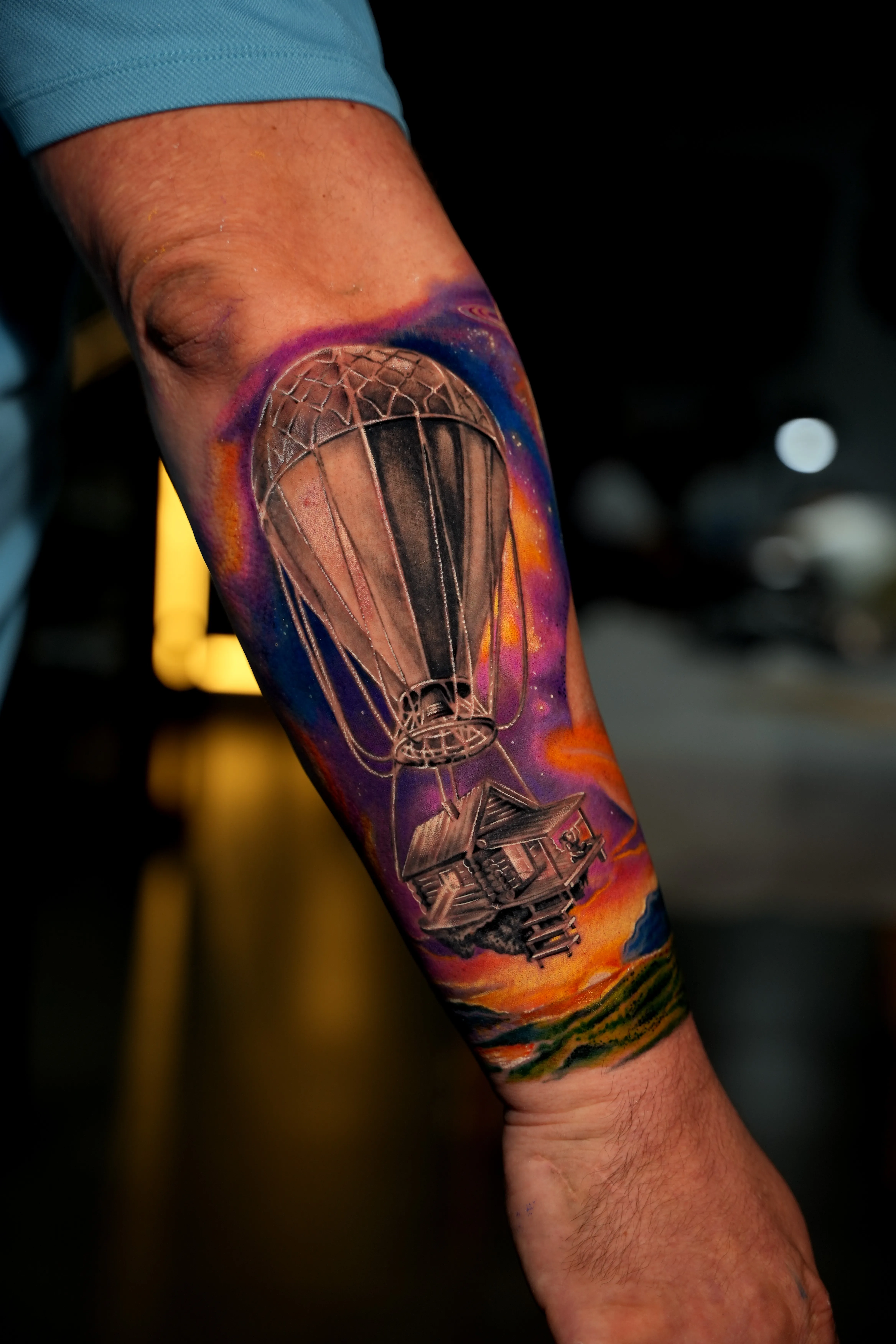 TKO Tattoo surreal color realism — a hot-air balloon lifting a wooden cabin over a vivid sunset