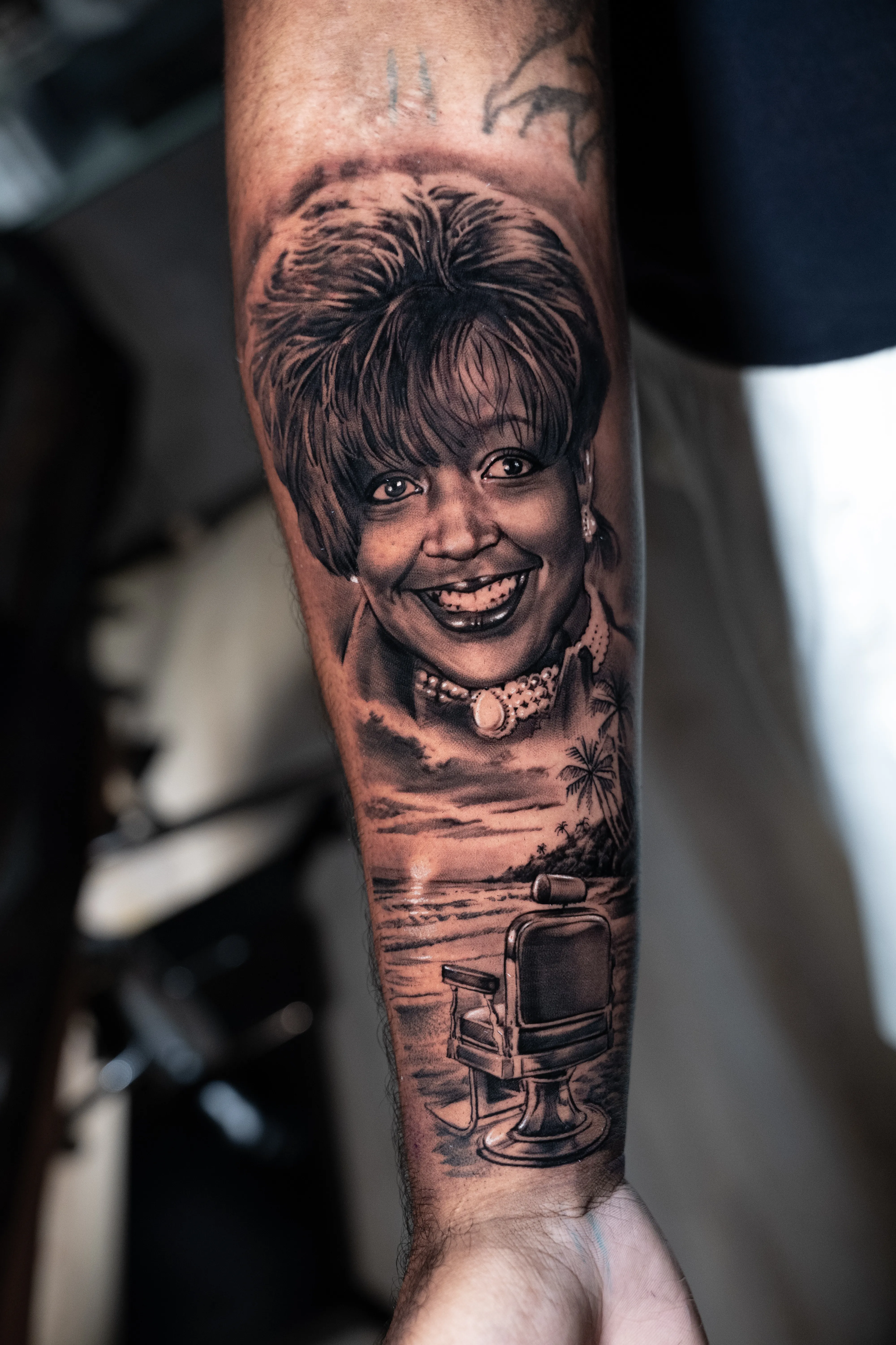 Black-and-grey portrait tattoo of a smiling woman with a beach and barber-chair scene — TKOTATTOO Fort Lauderdale